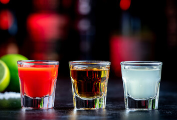 Golden tequila with sangrita and lime juice. Black bar counter background, steel bar tools and bottles