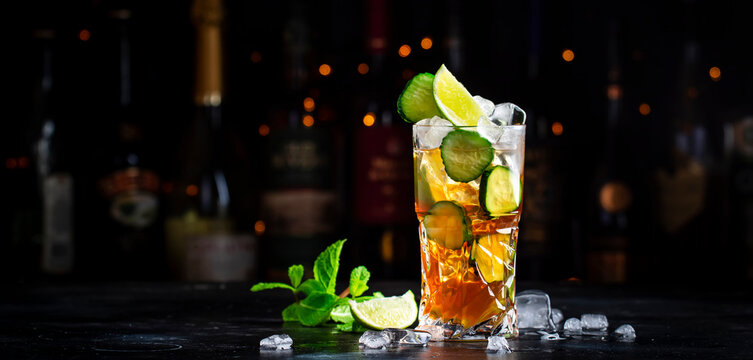 Pimms with cucumber, lime and ice - alcoholic cocktail drink with vodka, ginger beer and lemon juice, dark bar counter background, copy space.
