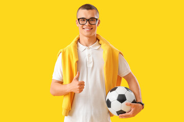 Male student with soccer ball showing thumb-up on yellow background