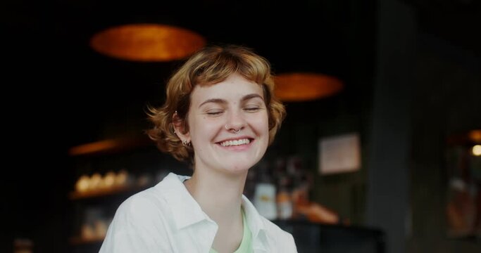 A young woman with earrings in her nose and ears smiles looking at the camera while sitting in a cafe