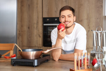 Young man with apple in kitchen