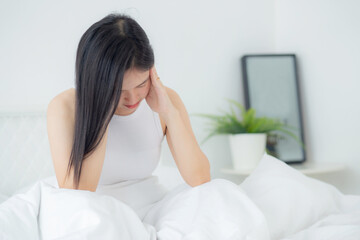 Young asian woman sitting on bed pain headache in the bedroom at home, unhappy female exhaustion...