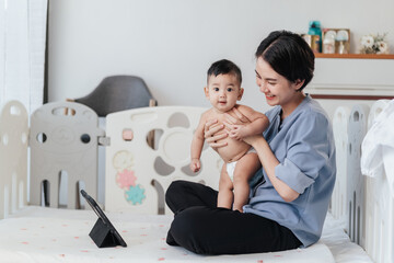 A boy Asian baby in mother's arms, excited and joyful use digital tablet with video calls with father or long-distance relatives. Tech-Fueled Family Love Concept.