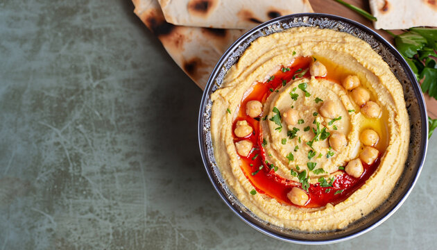 Hummus. Large bowl of homemade hummus garnished with chickpeas, red sweet pepper, parsley and olive oil, flat lay, middle east food