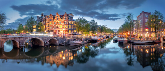 Amsterdam. Panoramic view of the historic city center of Amsterdam. Traditional houses and bridges of Amsterdam. A blue evening time and the serene reflection of lights in the water. Long exposure. Eu - obrazy, fototapety, plakaty