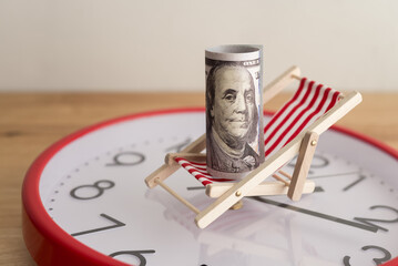 US dollar bill banknote on beach chair and red clock wooden table background. Concept of dividend yield in long term investment trading, passive income freedom, money savings for retirement.