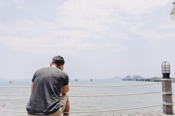 Single lonely asian man sitting alone looking out to the sea bay.