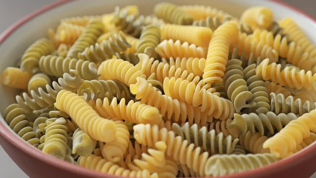Multicolor raw pasta fusilli in a bowl. Rotating table