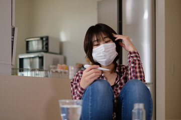 体調不良で体温計で熱を計る若い女性