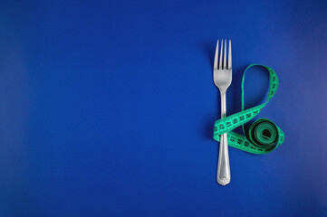 Measuring tape threaded through a fork on a blue background. Good proper nutrition. Medical fasting. The concept of a diet for weight loss. Healthy lifestyle