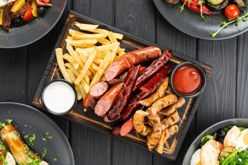 grilled sausages french fries ketchup and mayonnaise sauce on cutting board on wooden background,...