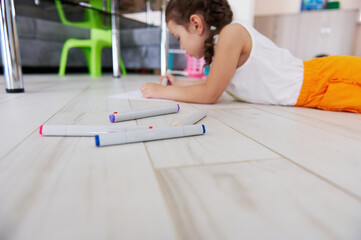 Felt-tip-pens, watercolor markers on the background of creative little child girl lying on the floor and drawing picture