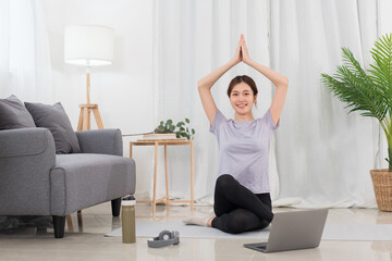 Fototapeta na wymiar Yoga exercise concept, Asian woman raising arms over head in lotus position while doing yoga online