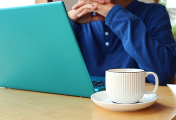 Closeup of a cup of coffee with a man working on laptop in the backdrop