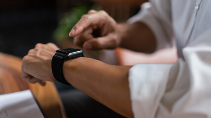 Hands of businessman checking time on smartwatch while working about financial document of business