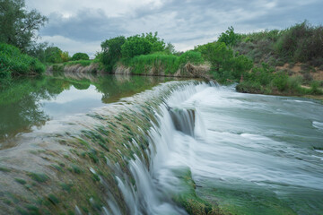 waterfall in a dam of a mountain river of crystalline waters with green vegetation, silk effect