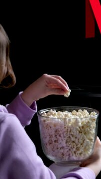 teenage sits on floor watches netflix on big screen of TV screensaver flashes on black background in red blue in hands young woman popcorn 