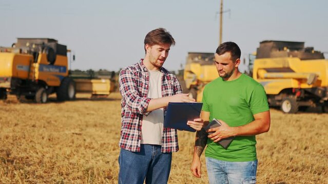 Farmer, logistics agent sign agreement on grain supply, shake hands in wheat field near harvesters. Agronomist discuss agriculture business contract. Rancher, landlord negotiate with handshake.