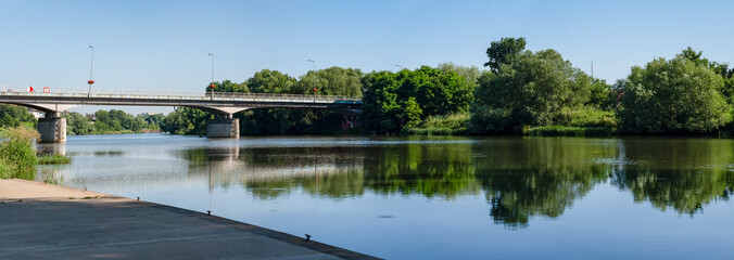 Panorama rzeki Odry w tle most lekko pochmurna pogoda, błękit nieba zieleń przy brzegu, pora letnia, Odra w odcinku województwa Opolskiego