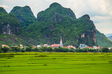 distant view of a church in a village with rice fields in front and high green mountains behind