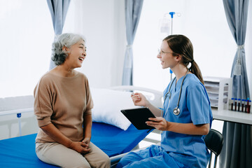Obraz premium Friendly Female Head Nurse Making Rounds does Checkup on Patient Resting in Bed. She Checks tablet while Man Fully Recovering after Successful Surgery in hospital.