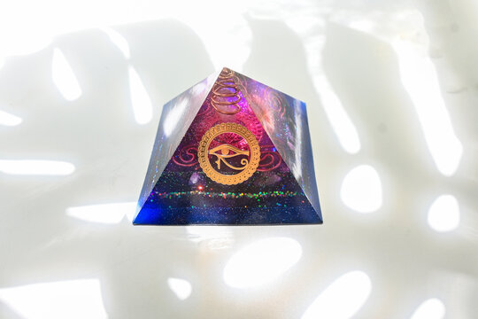 Violet navy blue gold and orange pink with eye of Horus and Yantra's and Mandalas Orgone Orgonite pyramid in shadow with natural background energy healing concept , counteract with efm