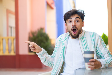 Handsome Arab man holding a take away coffee at outdoors surprised and pointing finger to the side