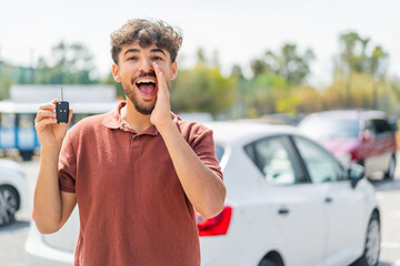 Fototapeta premium Young Arabian handsome man holding car key at outdoors shouting with mouth wide open