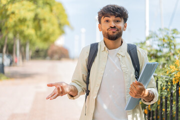 Young student Arabian man at outdoors making doubts gesture while lifting the shoulders