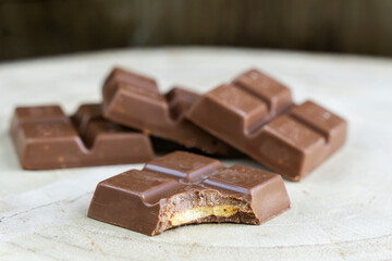 Organic dark and mil chocolate squares on a slate tray with monstera leaves in the background. One of de pieces is bitten.