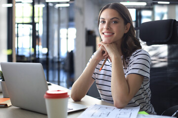 Beautiful young woman is sitting in the office and looking at camera.