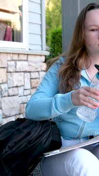 portrait of girl holding a bottle of water and drink, wearing school uniform and blue backpack sit on the floor against the grey wall. High quality photo