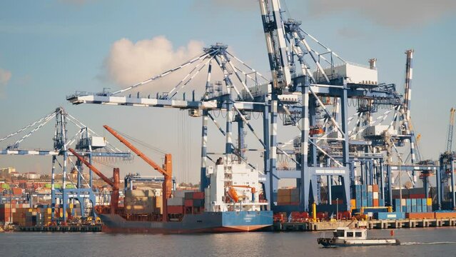 4K footage from commercial port area. Huge port crane structure by the sea. Crane lifting container from docked vessel and small boat passing by the port stock video.