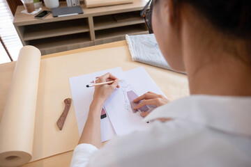 Young female fashion designer sketching at studio desk.