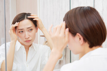 Obraz na płótnie Canvas 洗面室で髪の毛を気にするミドルエイジの女性