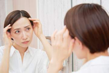 洗面室で髪の毛を気にするミドルエイジの女性