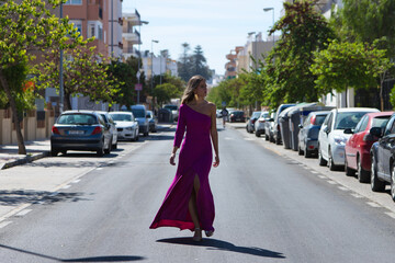 Young beautiful blonde woman dressed in purple dress walks along a large lonely avenue among the...