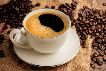 Black coffee or hot tea in a cappuccino espresso cup, breakfast food with coffee beans on a wooden table Isolated on a dark background, top view