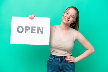 Young caucasian woman isolated on green background holding a placard with text OPEN with happy expression