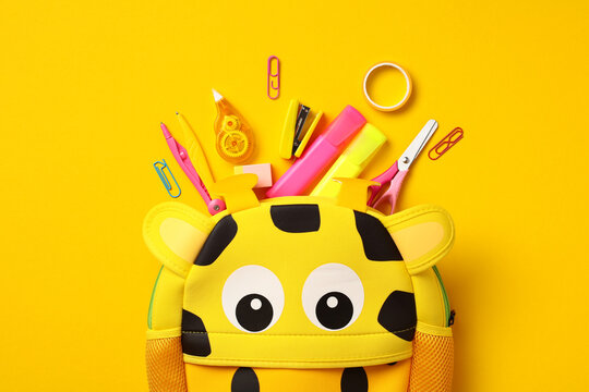 Kids backpack giraffe with school stationery on yellow background. Back to school concept. Flat lay, top view, overhead.