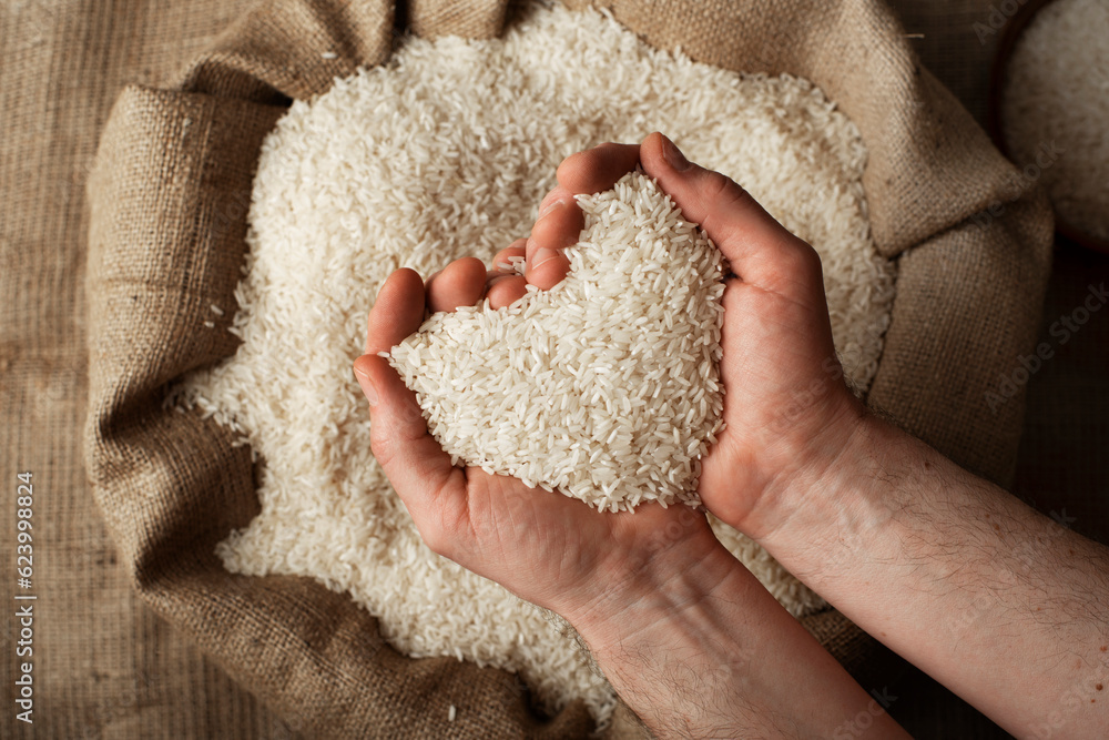 Wall mural human hands in shape of heart holding handful of rice over burlap sack