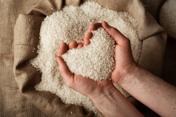 Human hands in shape of heart holding handful of rice over burlap sack