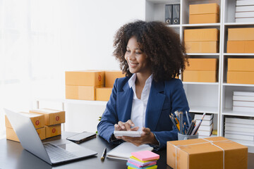 Happy African American businesswoman owner with a parcel box and checking orders from customers, online delivery service warehouse, sell products online concept.