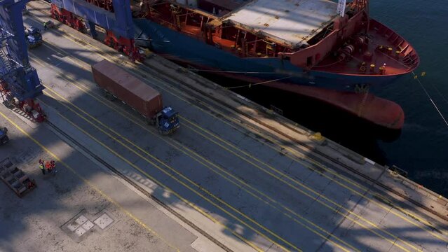 4K aerial footage over port. Drone following cargo trailers carrying containers unloaded from docked freight ship stock video. 