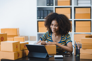 African American owner checking orders from customers sitting at desk in office, sell products online concept.