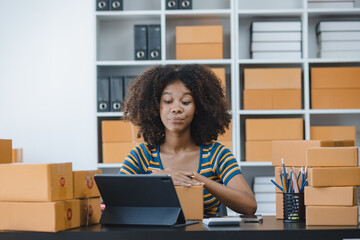 African American owner checking orders from customers sitting at desk in office, sell products online concept.