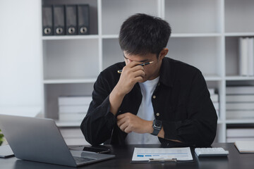 Asian businessman working online with laptop are stressed and tired from work sitting at desk in the office, feeling sick at work, stress from work.	