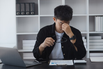 Asian businessman working online with laptop are stressed and tired from work sitting at desk in the office, feeling sick at work, stress from work.	