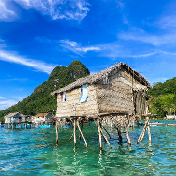 A picturesque Bajau Laut stilt house by the breathtaking backdrop of mountains and blue sky.