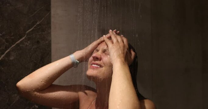 Beautiful woman takes shower while relaxing under running water in hot shower. Closeup of adult caucasian woman enjoying relaxation time in shower